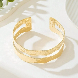 Detail of wide golden cuff bracelet featuring a textured hammered surface and dual-layer design