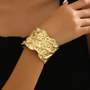Close-up of golden wide cuff bracelet featuring artistic hammered wrinkled texture