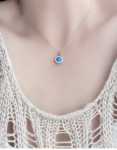 Macro close-up of a round blue opal pendant necklace with a halo of white zircons