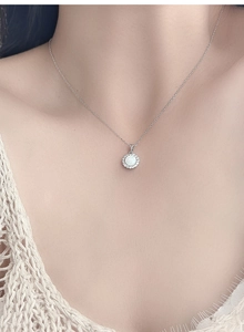 Close-up of a silver round white opal pendant necklace with shimmering zircon halo on a model