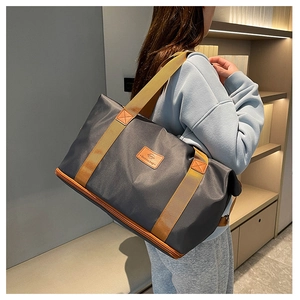 Detail of grey travel bag with brown straps worn by a model in a modern interior