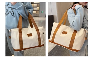 Close-up of a large beige travel tote with brown straps and leather logo patch