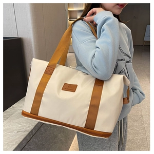 Detail of expandable cream travel tote with brown leather handles and fashion logo