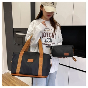 Detail view of the black and brown expandable travel bag set held by a model in a home setting