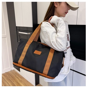 Detail shot of a black waterproof travel bag with tan straps worn by a woman