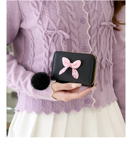 Close-up of black mini wallet with pink polka dot bow and plush ball charm in hand