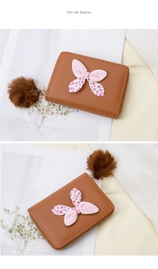 Detail of brown PU leather wallet featuring a polka dot bow and plush pompom charm