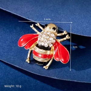 Detail showing dimensions of bee brooch with red wings and crystals on blue paper