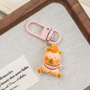 Cute orange cartoon bear keychain with pink lobster clasp on decorative textile background