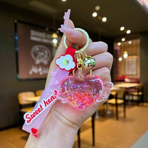 Dettaglio portachiavi a cuore alato con glitter rosa, campanello dorato e ciondoli a fiore