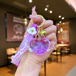 Dettaglio portachiavi a cuore viola con ali, glitter liquidi e campanello metallico oro