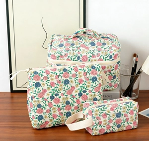 Three-piece floral cotton makeup bag set with top handle and zippers on wooden desk