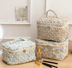 Three quilted cotton floral cosmetic bags with dual zippers and handles on a wooden table