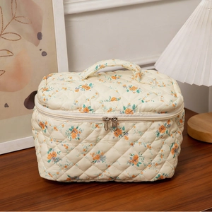 Floral quilted makeup bag with handle and zipper on a wooden table, cozy home decor