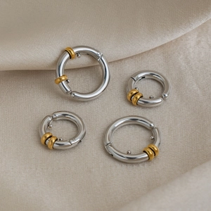 Détail macro de créoles polies en argent et or sur un tissu élégant en soie beige