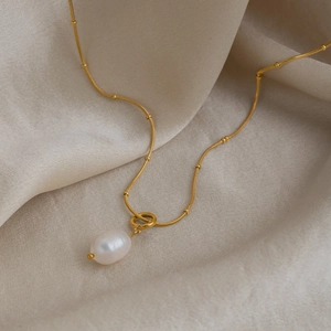 Detailed close-up of a golden snake chain necklace with a white teardrop pearl pendant