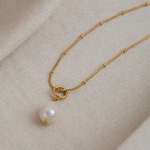 Detail shot of a white freshwater pearl pendant on a gold-beaded snake chain necklace