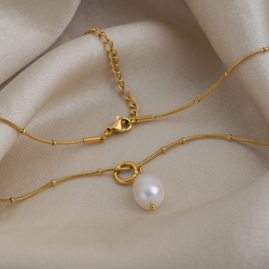 Detailed close-up of a gold freshwater pearl pendant necklace on soft silk background