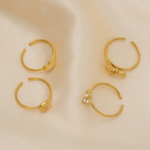 Four-piece gold plated adjustable rings with heart, rose, and bow designs on beige silk