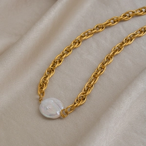 Detail of a gold chunky chain necklace with a large irregular baroque pearl on silk