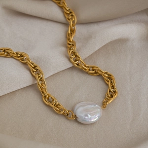 Gold stainless steel woven necklace featuring a natural baroque pearl on beige fabric
