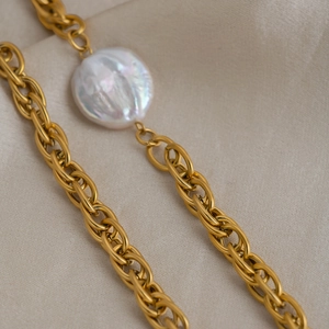 Detailed shot of a gold chain necklace with a large baroque pearl on a beige linen fabric
