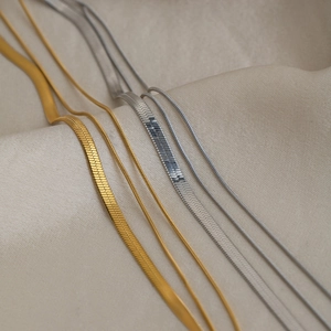 Close-up of layered gold and silver flat herringbone and round snake chains on fabric