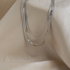 Detailed close-up of triple-layered silver snake chain necklaces on beige fabric