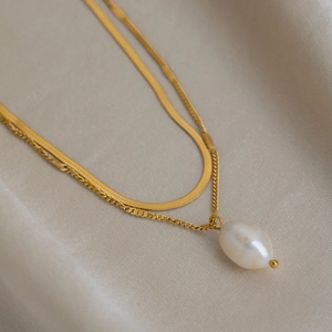 Detail of gold double-layered necklace featuring sleek snake chain and baroque pearl pendant