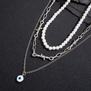 Three-piece silver necklace set featuring blue evil eye pendant, barbed wire link and pearls