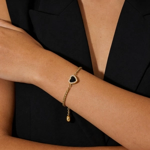 Close-up of golden heart bracelet with black pendant and sparkling zircons on a wrist
