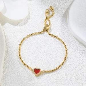 Close-up of golden bolo bracelet with red enamel heart and zircon stones on ceramic base
