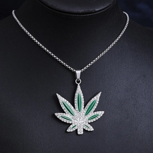 Detailed shot of green enamel maple leaf pendant with diamonds on a black display stand