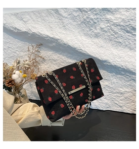 Detail of strawberry print corduroy bag with gold chain strap and metal trim closure