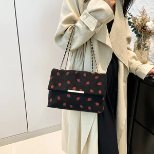 Detail of black corduroy shoulder bag with red strawberry print and gold chain strap