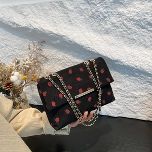 Detail of black corduroy shoulder bag with red strawberry print and gold chain strap