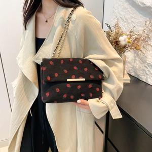 Chic black corduroy shoulder bag with strawberry print and gold chain strap on a model