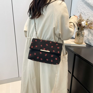 Detail of black corduroy shoulder bag with strawberry embroidery and gold chain strap