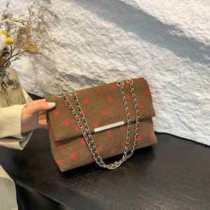 Detailed close-up of brown corduroy fabric with red strawberry print and chain strap
