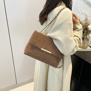 Detail of strawberry embroidery on brown corduroy chain bag worn by a model