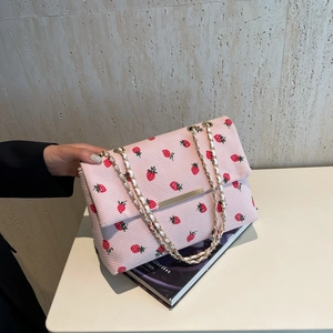 Close-up of pink corduroy shoulder bag with red strawberry pattern and gold chain