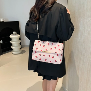 Detailed shot of pink crossbody bag featuring red strawberry prints and gold chain strap