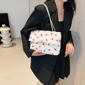 Detail of a white rectangular shoulder bag with red strawberry print and gold chain strap