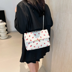 Detail of white strawberry print bag with gold chain strap on a model's shoulder