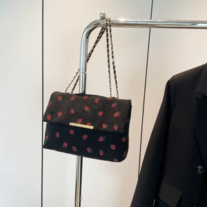 Detail of black corduroy shoulder bag with red strawberry embroidery and gold chain