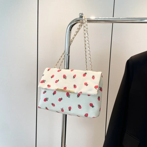 Close-up of white corduroy shoulder bag with strawberry print and gold chain strap