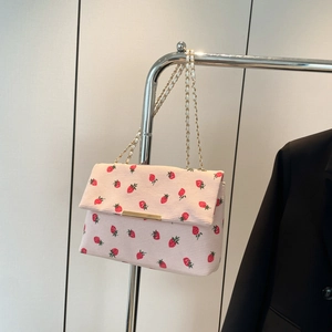 Detail view of pink corduroy shoulder bag featuring red strawberry prints and gold chain