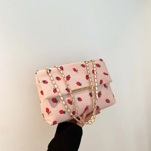 Detail of pink corduroy shoulder bag with red strawberry prints and gold metal chain