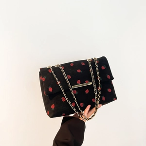 Close-up of black corduroy shoulder bag featuring strawberry prints and gold chain strap