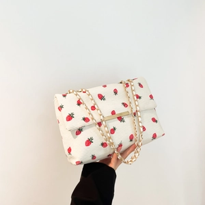 Detail of white corduroy shoulder bag featuring red strawberry prints and gold chain
